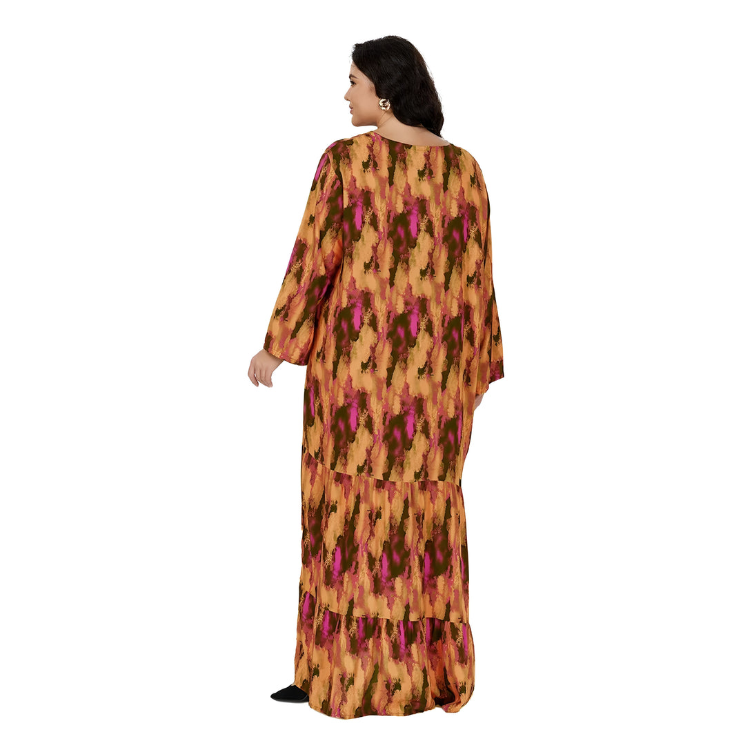 Une femme porte une longue robe à manches longues à imprimé orange, vert et rose. La robe est à volants et la femme regarde au loin.