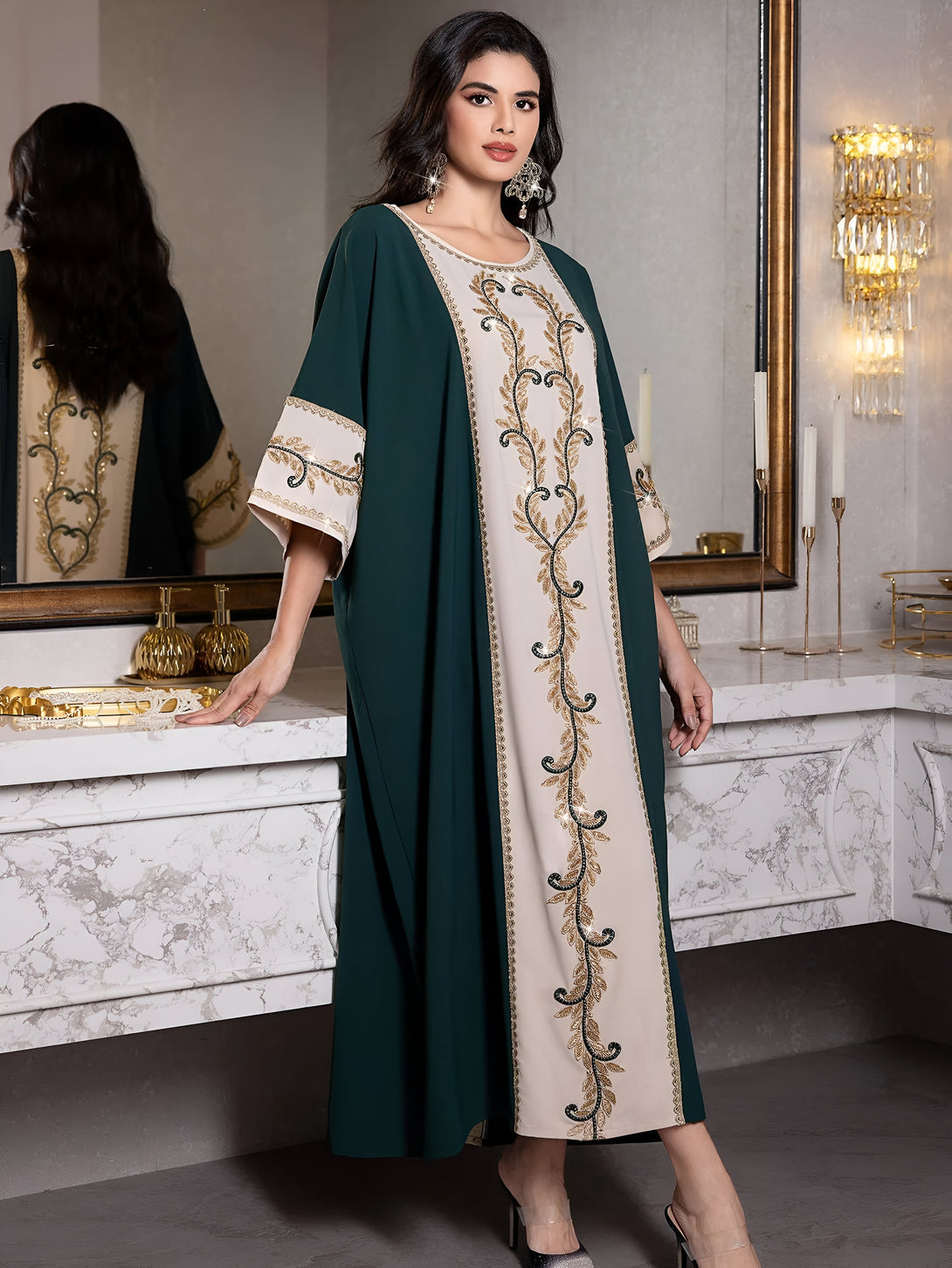 Une femme portant une robe verte avec des détails dorés et une bordure de feuilles dorées brodées. La robe est à manches courtes et arrive aux chevilles. La femme porte des talons hauts transparents. La robe est élégante et parfaite pour les occasions spéciales.
