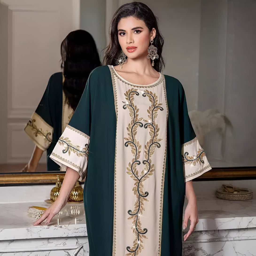 Une femme porte une abaya verte avec des détails dorés et des broderies brillantes. La robe est à manches longues et est parfaite pour les occasions spéciales.