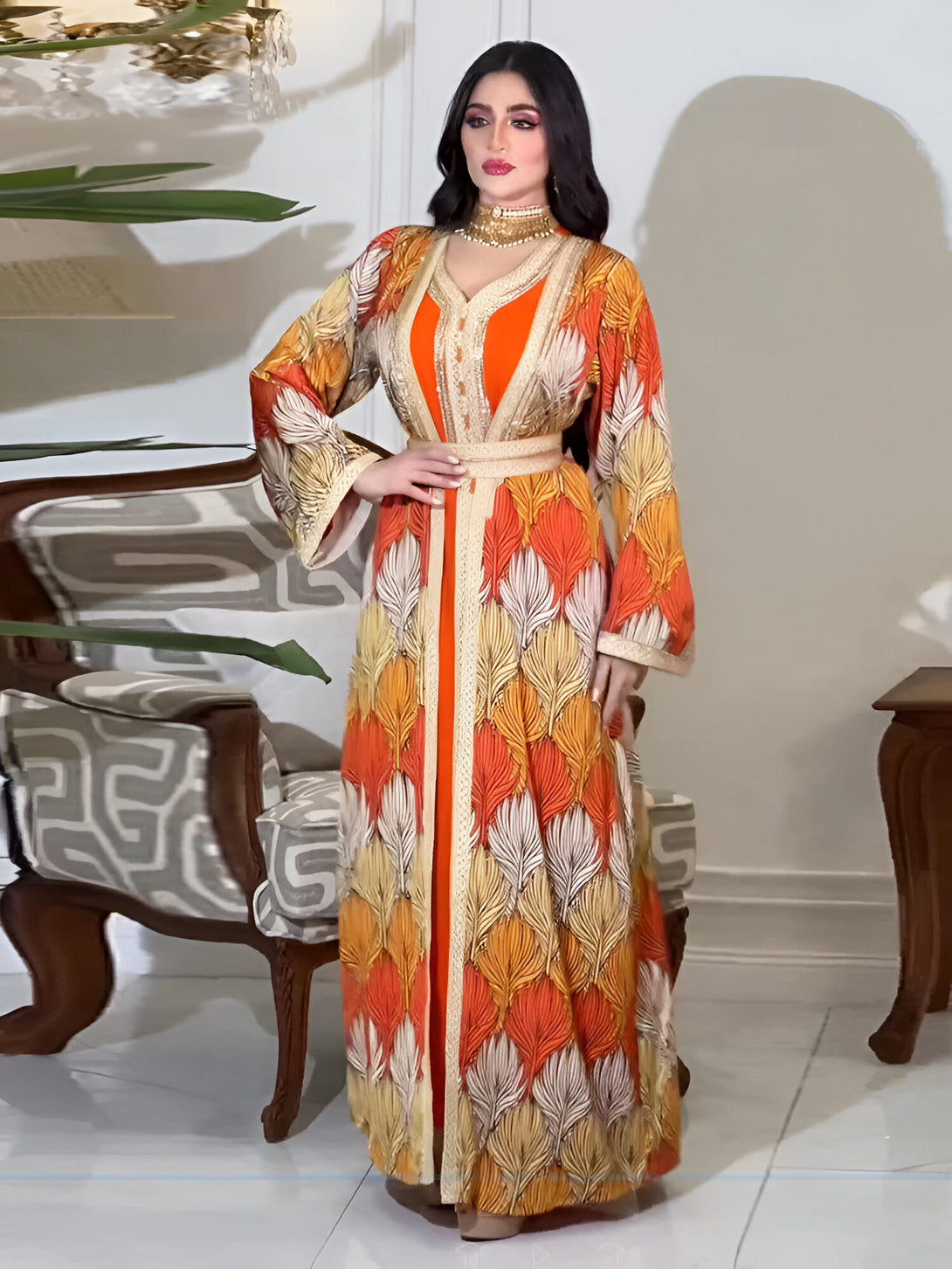 Une femme portant une longue robe orange et blanche à motifs de plumes avec une ceinture dorée.  La robe est élégante et modeste, parfaite pour les occasions spéciales.