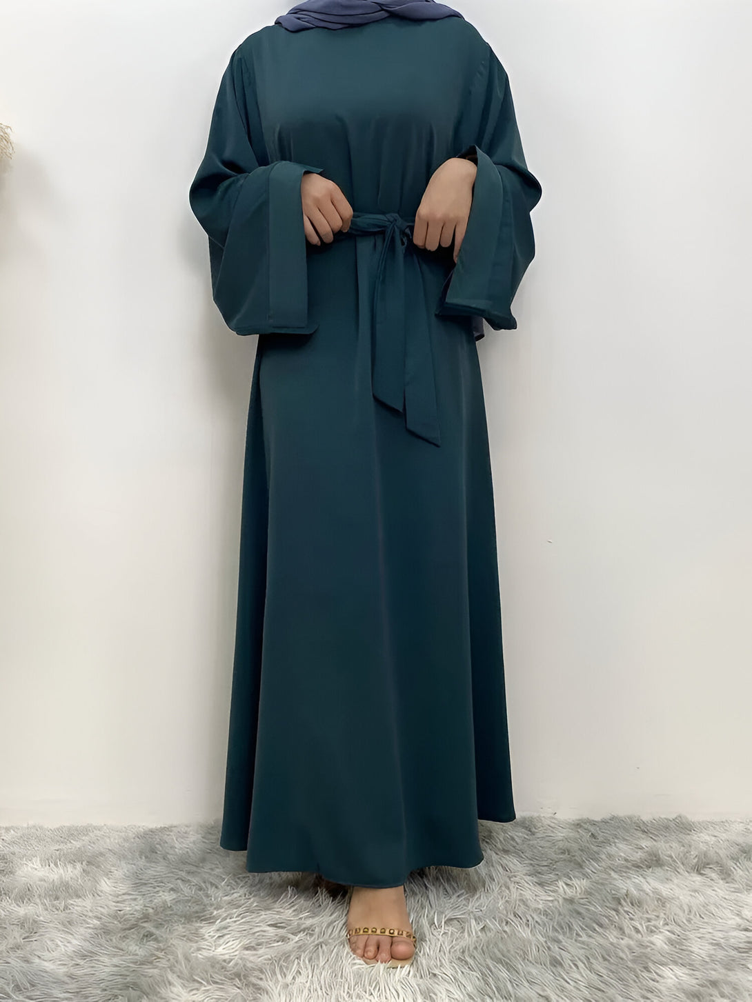 Une femme porte une abaya verte à manches larges avec une ceinture assortie. La tenue est élégante et confortable, idéale pour les occasions spéciales ou le quotidien.