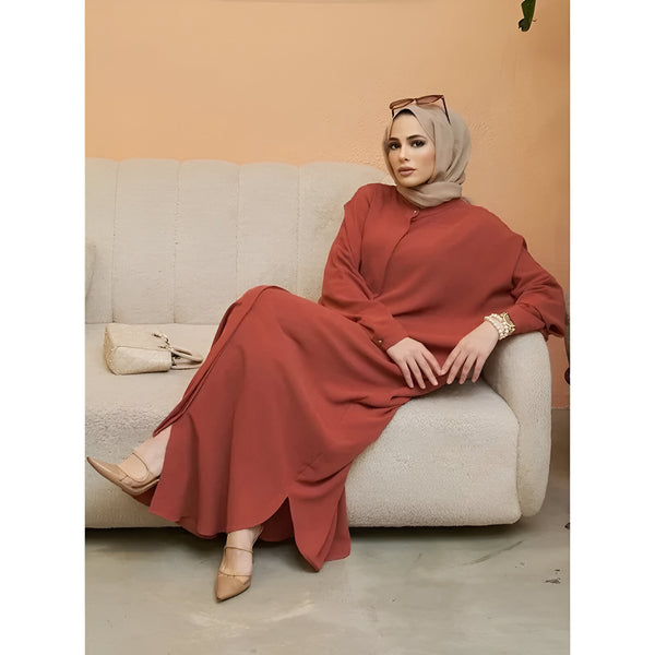 Une femme portant une robe longue rouge et un hijab beige, assise sur un canapé beige.