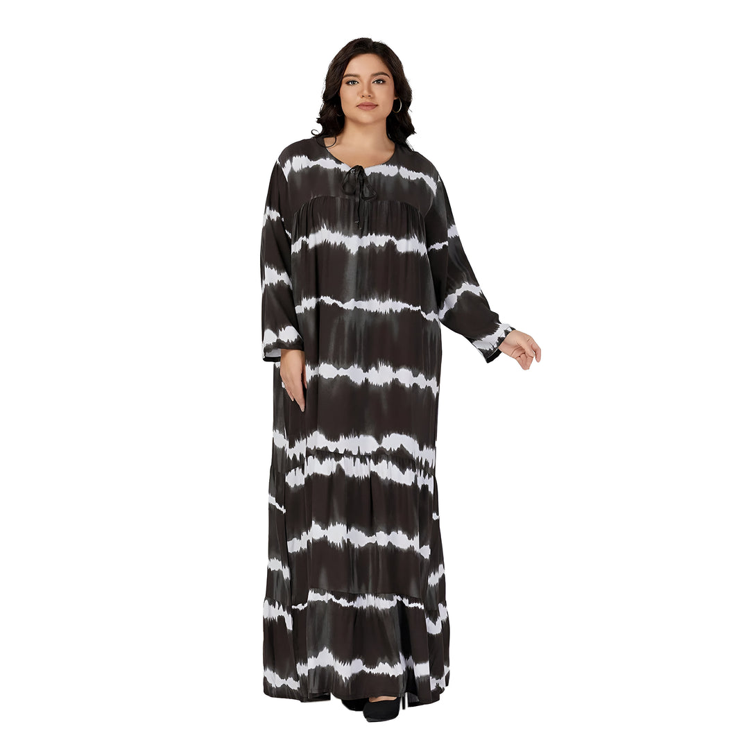 Une femme porte une longue robe noire et blanche à manches longues avec un motif tie-dye. La robe est ample et a une coupe décontractée. Elle est idéale pour les occasions décontractées ou habillées.