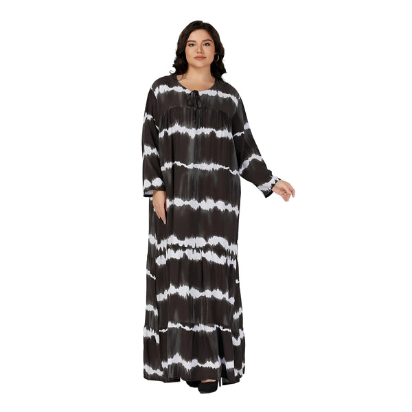 Une femme porte une longue robe noire et blanche à manches longues avec un motif tie-dye. La robe est ample et a une coupe décontractée. Elle est idéale pour les occasions décontractées ou habillées.