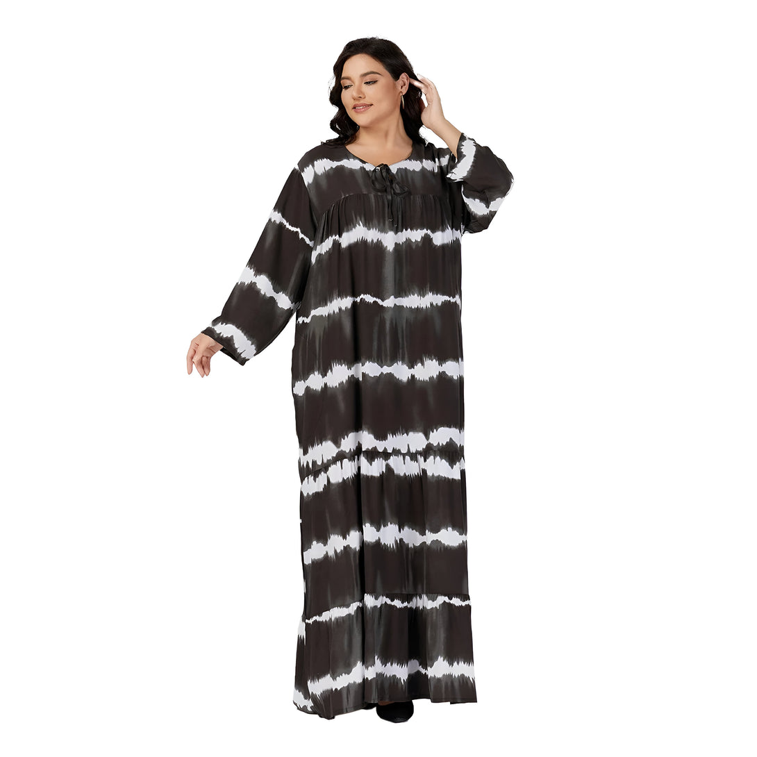Une femme porte une robe longue noire à rayures blanches et tie-dye. La robe est ample et confortable, parfaite pour les occasions décontractées.
