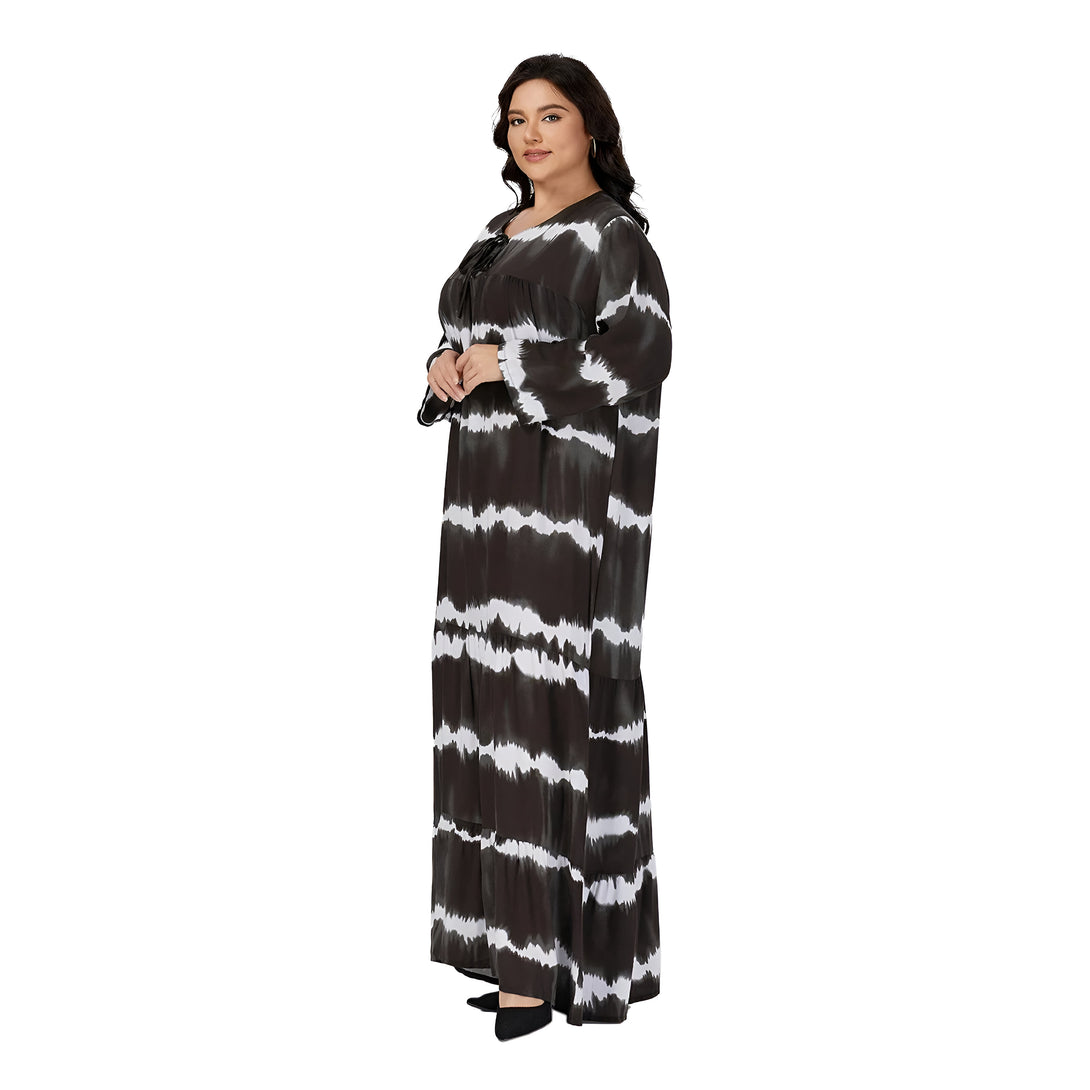Une femme porte une robe longue noire à rayures blanches. La robe a un décolleté en V et des manches longues. La femme porte des chaussures noires.