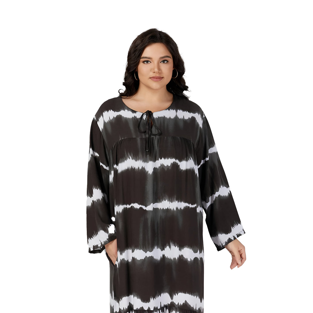 Une femme porte une robe noire et blanche à imprimé tie-dye avec un col rond et des manches longues. La robe a un cordon à la taille et des poches sur les côtés.