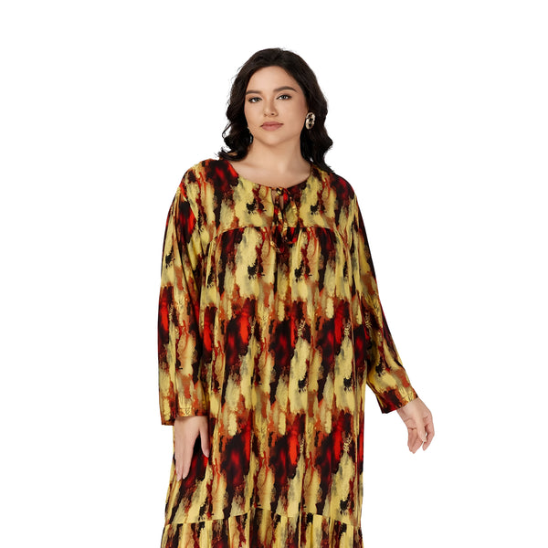 Une femme porte une robe longue à manches longues avec un motif abstrait jaune, rouge et noir. La robe est cintrée à la taille et a un col rond. La femme a les cheveux bruns et porte des boucles d'oreilles dorées.
