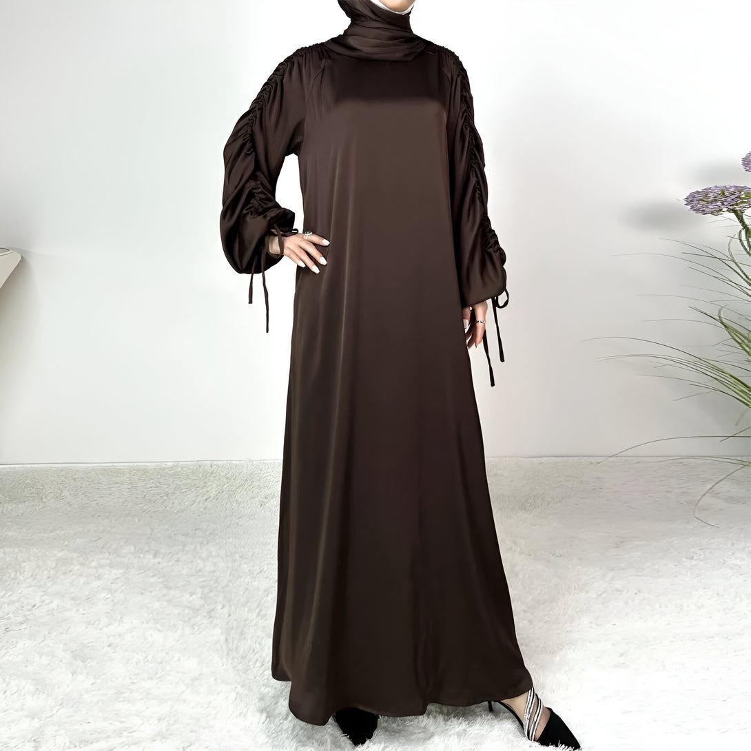 Une robe longue en satin marron avec des manches bouffantes et des lacets. La robe est idéale pour les femmes musulmanes.
