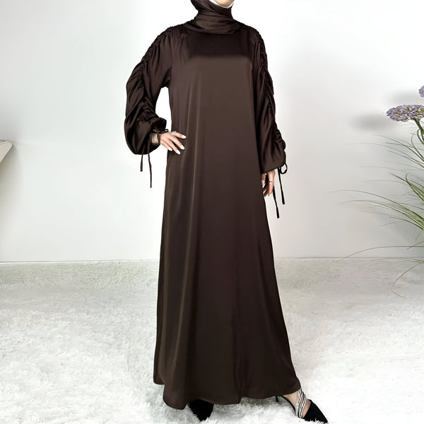 Une robe longue en satin marron avec des manches bouffantes et des liens.  La robe a une coupe ample et est parfaite pour les occasions spéciales.