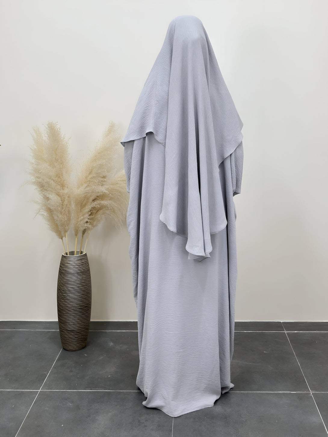 Une robe longue grise pour femme musulmane, avec un hijab assorti. La robe a un design ample et fluide, et le hijab est drapé sur la tête.