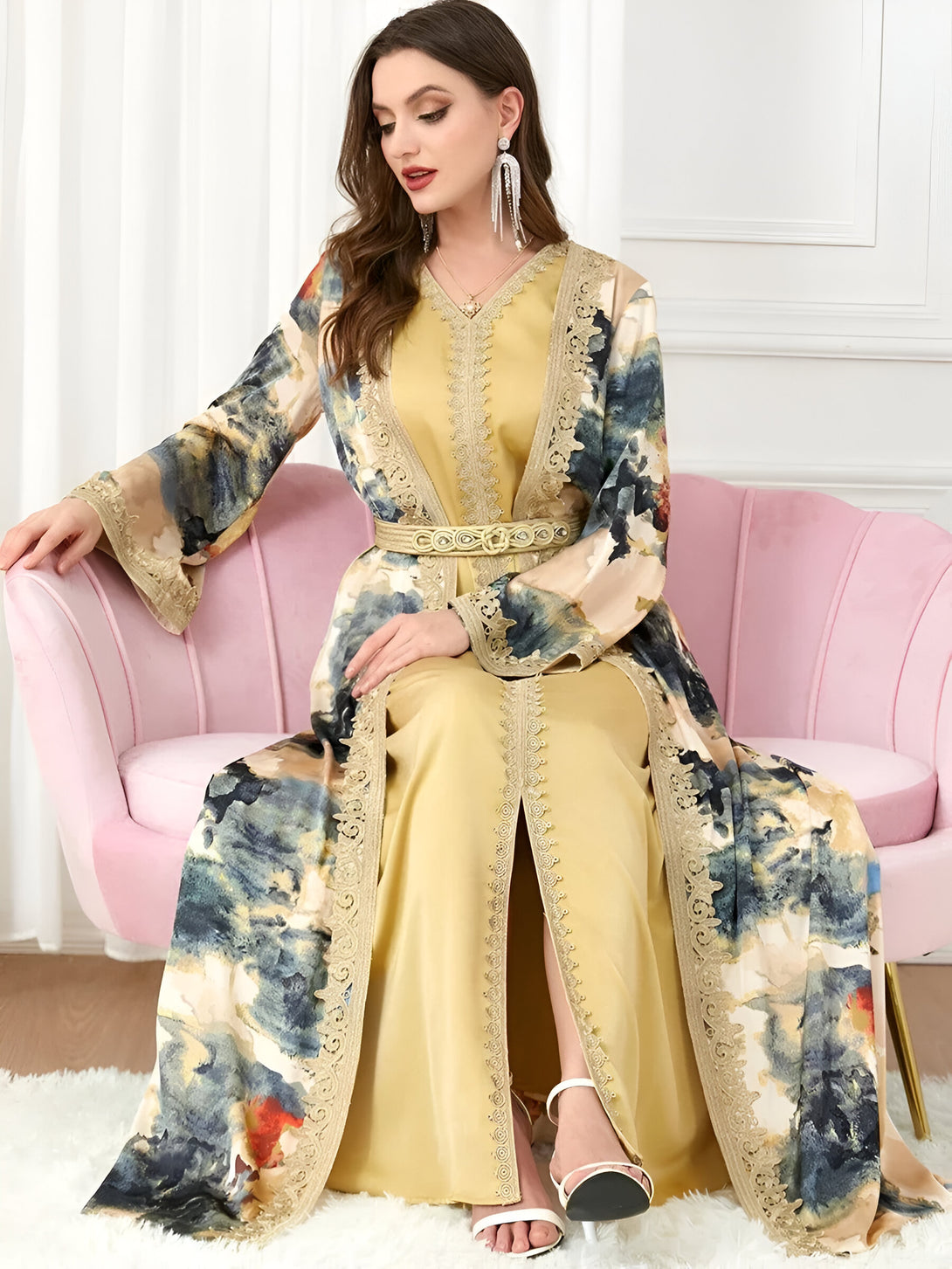 Une femme portant une longue robe jaune musulmane avec des détails en dentelle dorée et un imprimé floral. La robe est cintrée à la taille avec une ceinture dorée.