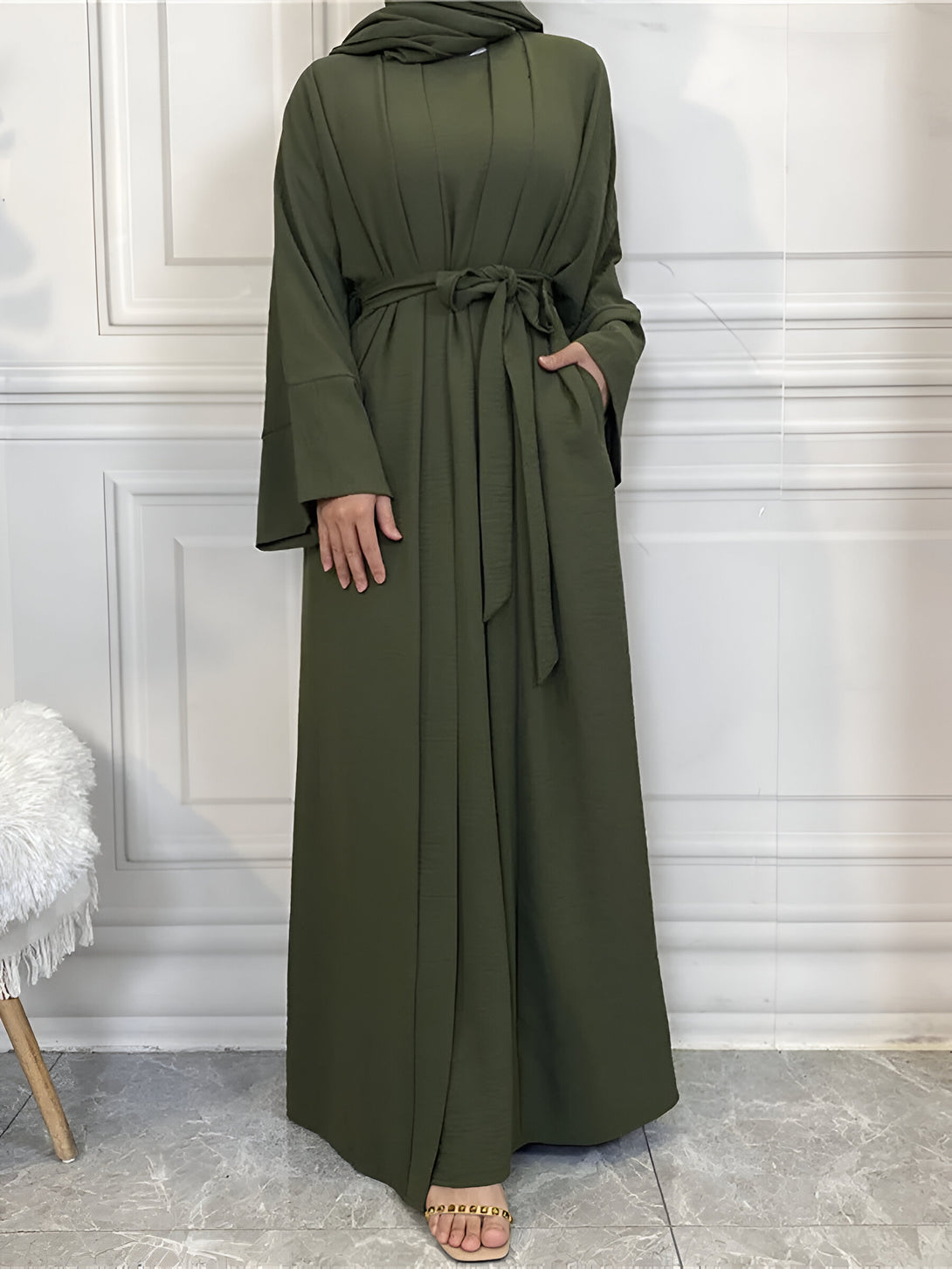 Une femme portant une longue robe verte à manches longues avec une ceinture. La robe est ample et élégante, parfaite pour une occasion spéciale ou un usage quotidien.