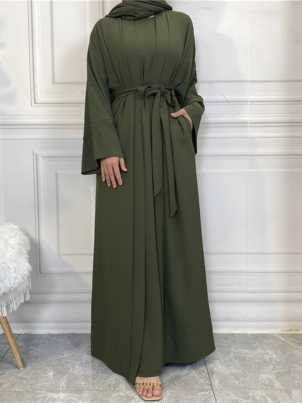 Une femme portant une longue robe verte à manches longues avec une ceinture. La robe est ample et élégante, parfaite pour une occasion spéciale ou un usage quotidien.
