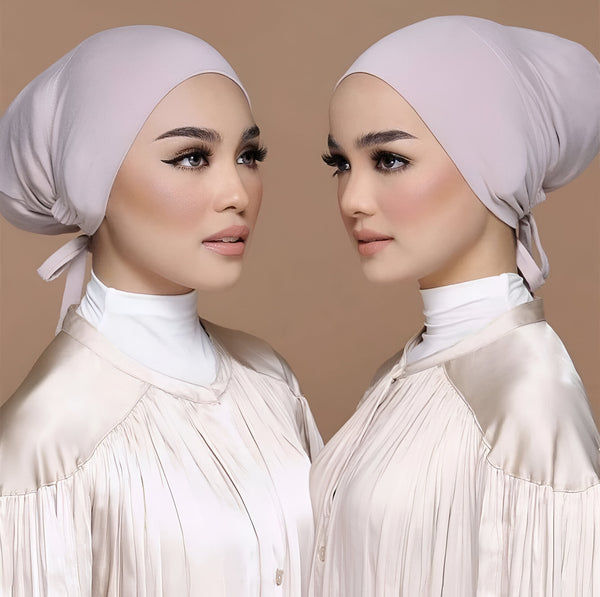 Deux femmes portant des hijabs beiges et des chemisiers blancs. Les femmes ont un maquillage subtil et regardent vers la droite.