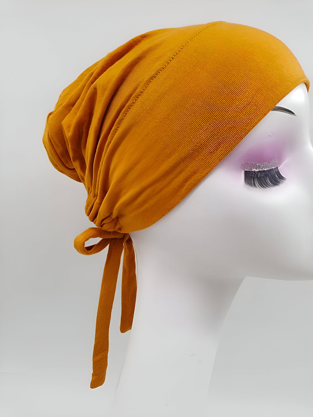 Un bonnet musulman en tissu extensible de couleur moutarde avec un cordon de serrage à l'arrière.