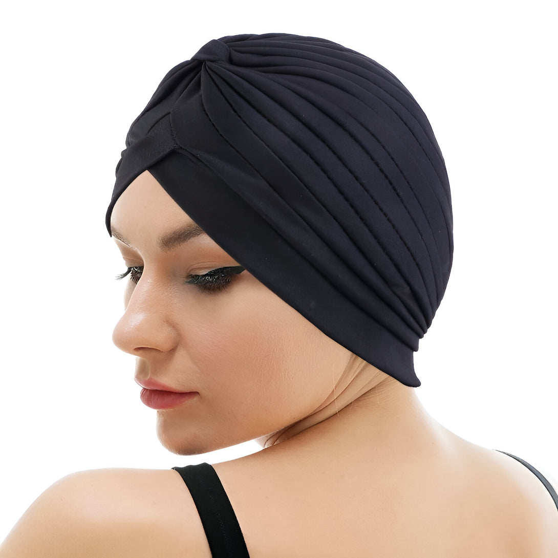 Une femme porte un turban noir élégant et moderne. Le turban est plissé et a un nœud élégant. Il est parfait pour un look chic et élégant.