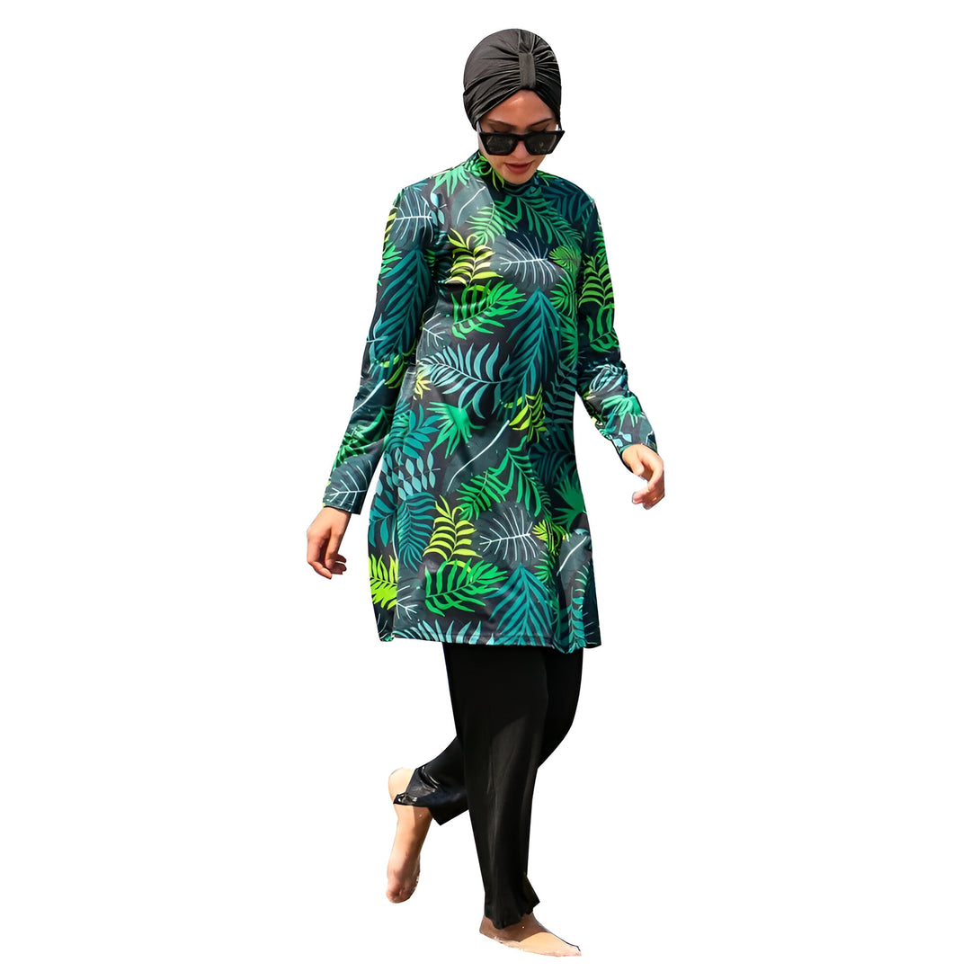 Une femme portant un maillot de bain musulman avec un imprimé tropical vert et noir.  Elle porte également un hijab noir et des lunettes de soleil.