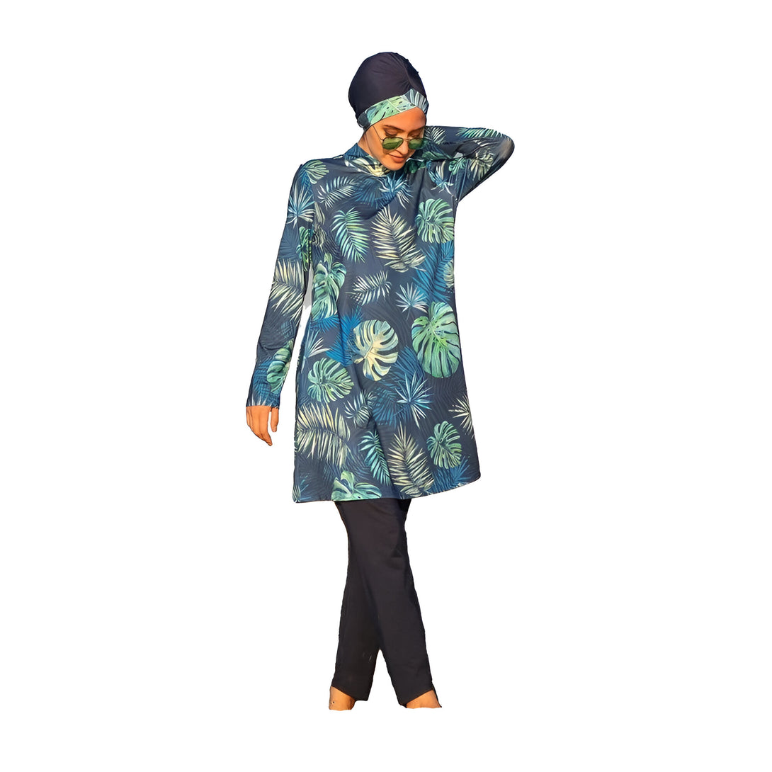 Une femme portant un maillot de bain musulman avec un motif de feuilles tropicales. Le maillot de bain est bleu marine avec des feuilles vertes et blanches. La femme porte également un foulard bleu marine.