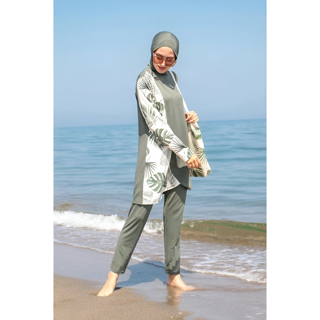 Une femme portant un maillot de bain musulman vert avec des feuilles imprimées sur le côté, debout sur une plage.
