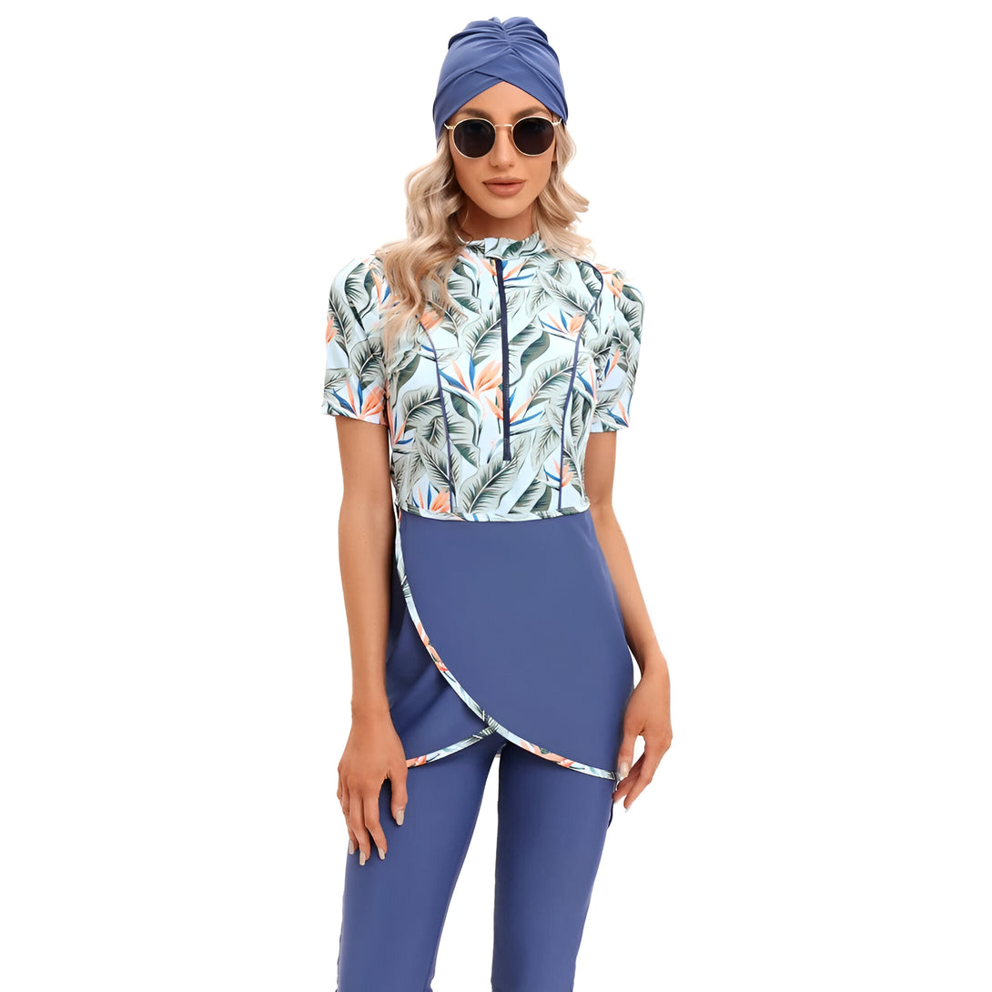 Une femme portant un maillot de bain musulman bleu avec un motif de feuilles tropicales. Elle porte également un foulard bleu et des lunettes de soleil.