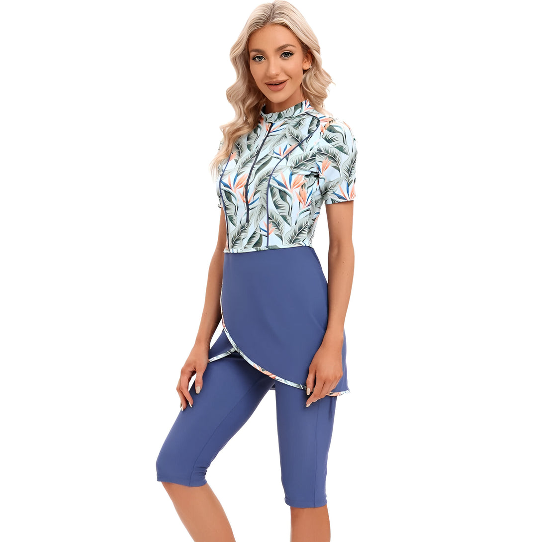 Une femme porte un maillot de bain musulman bleu marine avec un motif de feuilles tropicales. Le maillot de bain a un haut à manches courtes et une jupe courte.