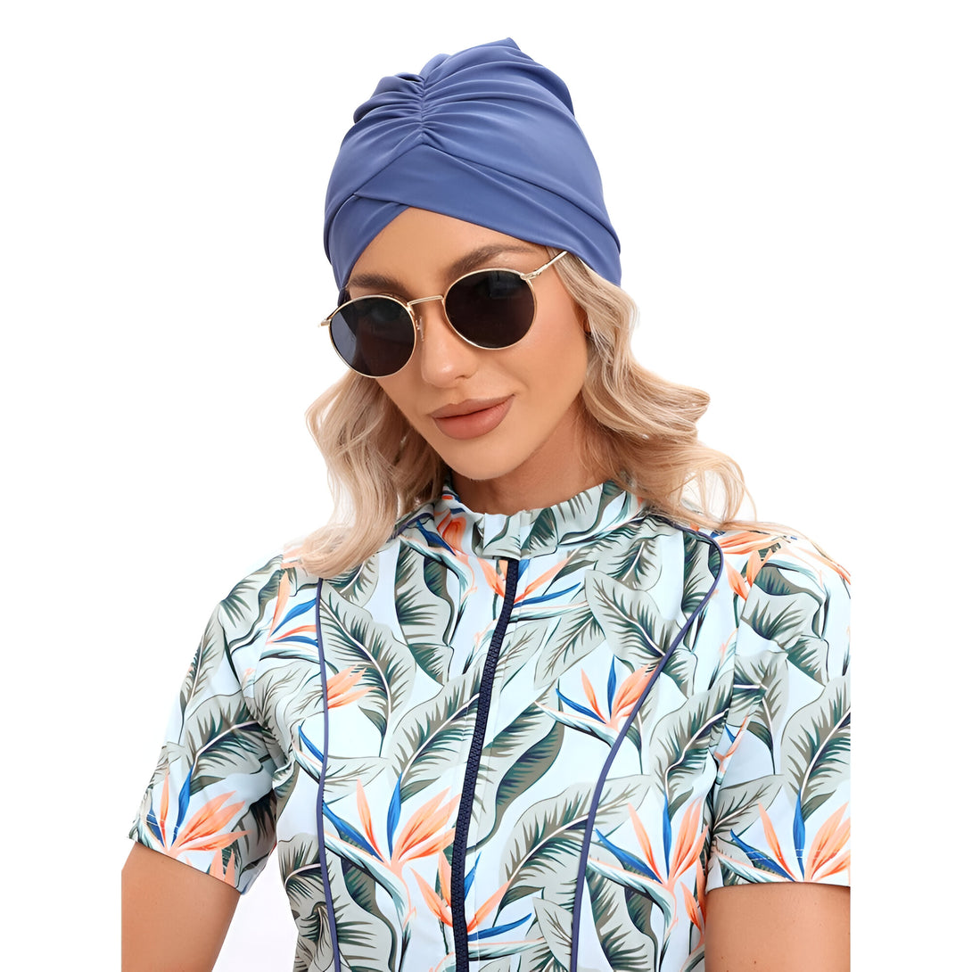 Une femme portant un hijab bleu et une robe de bain à motifs tropicaux, portant des lunettes de soleil.