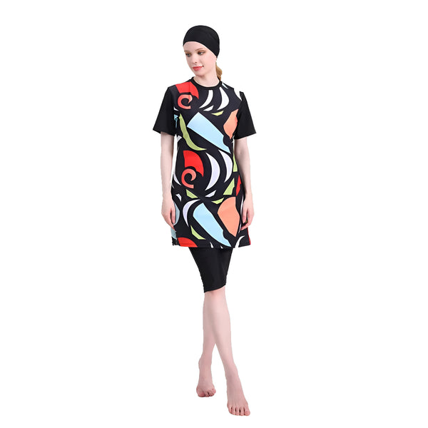 Une femme portant un maillot de bain musulman noir à motifs géométriques rouges, bleus, jaunes et oranges. Le maillot de bain comprend une tunique à manches courtes et un pantalon long. La femme porte un voile noir.