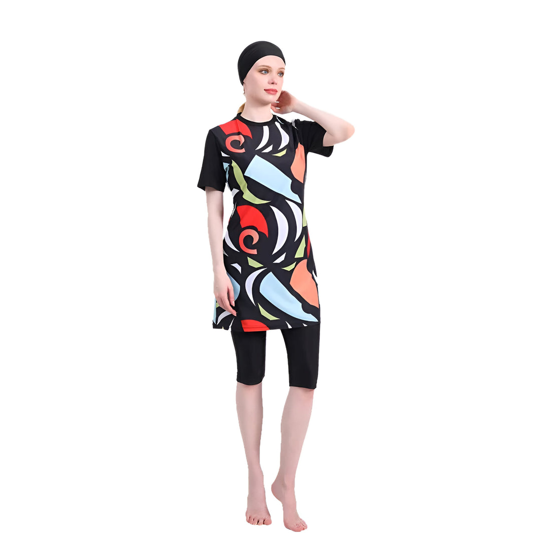 Une femme portant un maillot de bain musulman noir avec des imprimés géométriques colorés. Le maillot de bain comprend une tunique à manches courtes et un pantalon long. La femme porte également un foulard noir.
