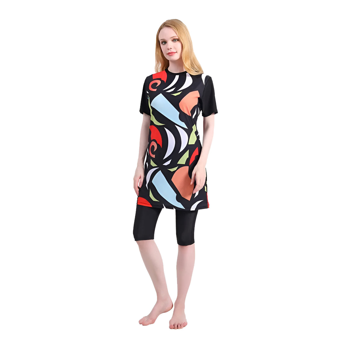Une femme portant un maillot de bain musulman noir avec un motif coloré.  Le maillot de bain a des manches courtes et une jupe longue qui couvre les genoux.  Le motif est abstrait et comprend des formes géométriques et des couleurs vives.