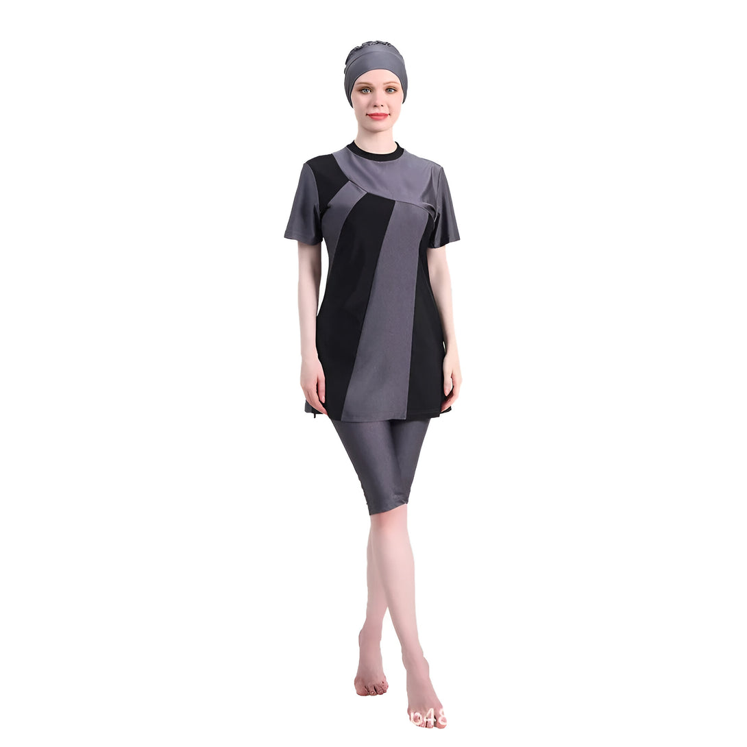 Une femme portant un maillot de bain musulman noir et gris avec une jupe et un pantalon de longueur genoux. Elle porte un foulard gris sur la tête.