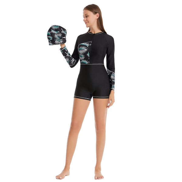 Une femme portant un maillot de bain musulman noir à manches longues avec un motif de feuilles vertes. Elle tient un bonnet de bain assorti à la main.