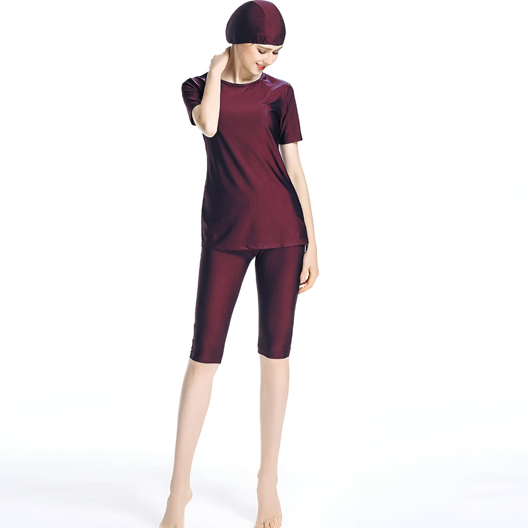 Une femme portant un maillot de bain musulman bordeaux avec un hijab assorti. Le maillot de bain est composé d'un haut à manches courtes et d'un pantalon long.
