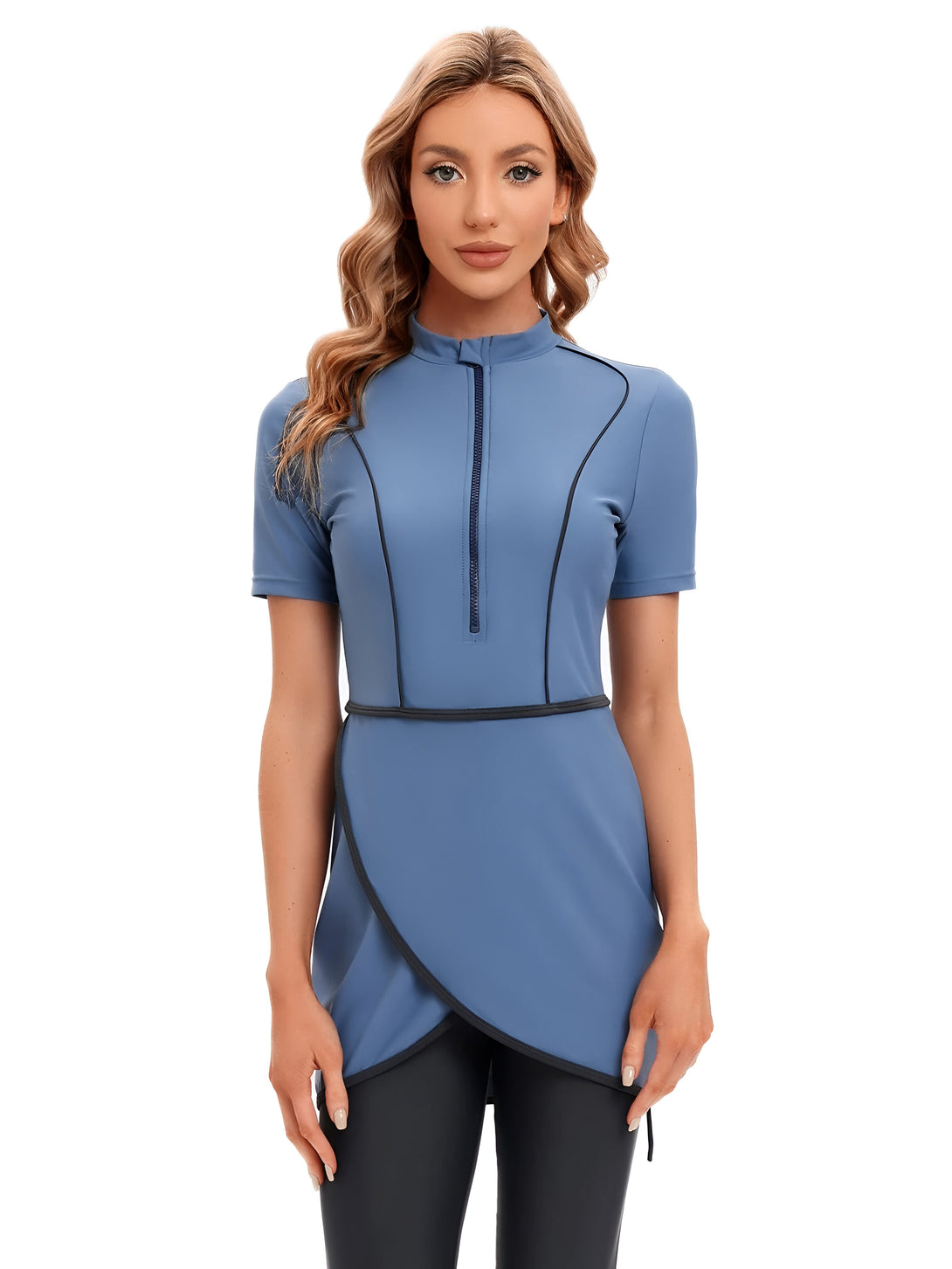 Une femme portant une robe de bain musulmane bleue avec une fermeture éclair sur le devant et une ceinture noire.  La robe de bain est à manches courtes et a un style enveloppant.  La femme a les cheveux blonds et porte un pantalon noir.
