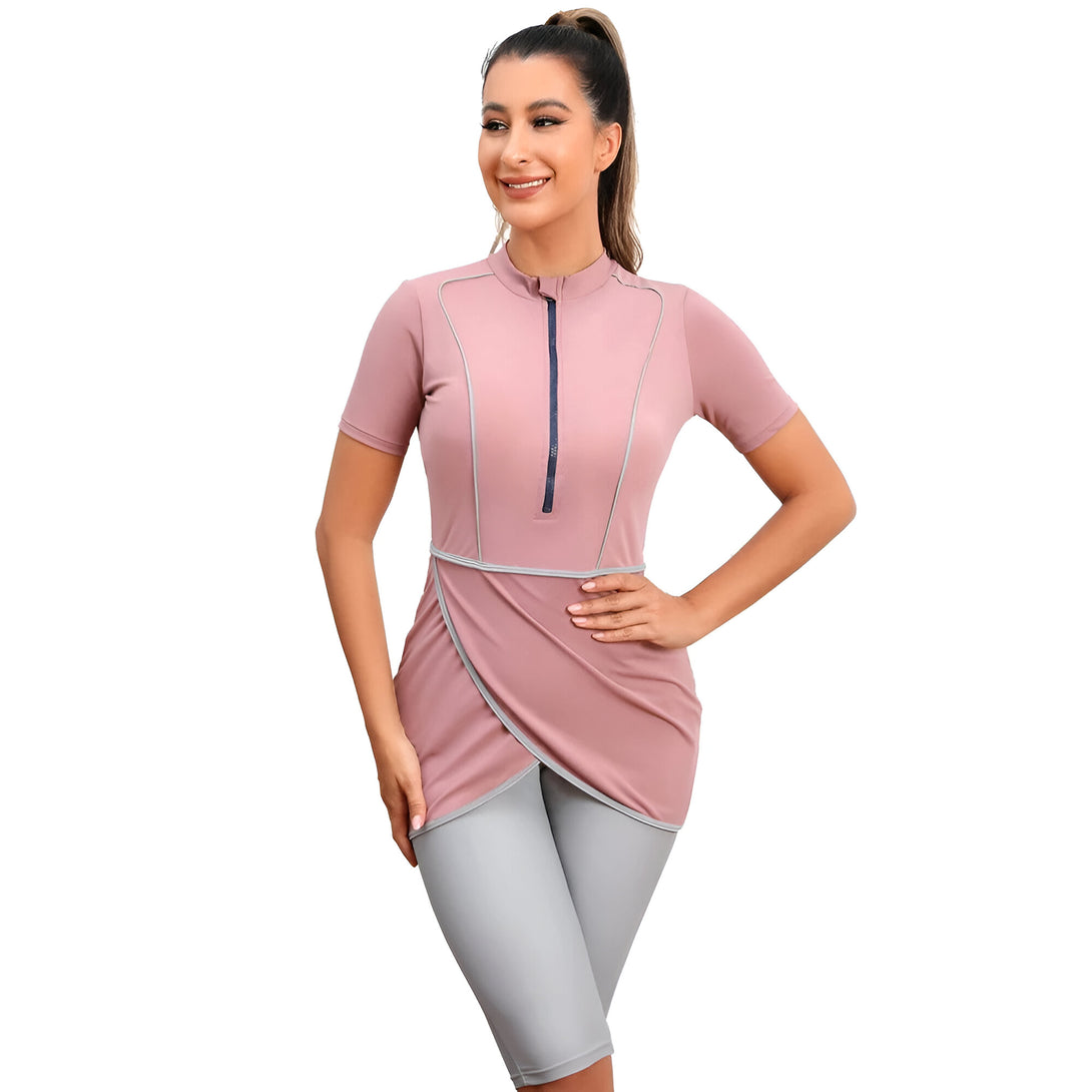Une femme porte un maillot de bain musulman rose avec une fermeture éclair et des détails gris. Le maillot de bain est à manches courtes et comprend un pantalon long.