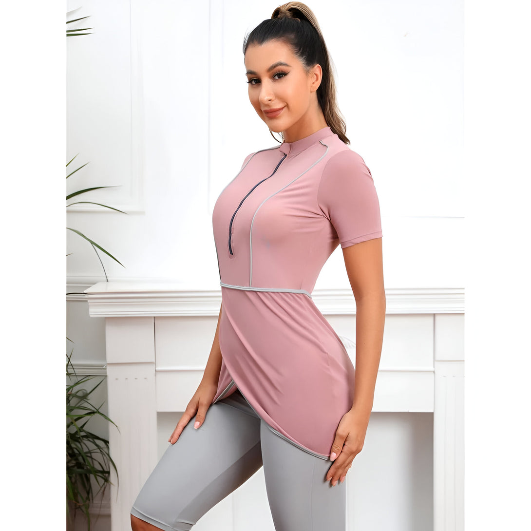 Une femme portant une tenue de bain musulmane rose et grise. La tenue de bain comprend un haut à manches courtes et un pantalon long. La tenue de bain est conçue pour être portée à la plage ou à la piscine.