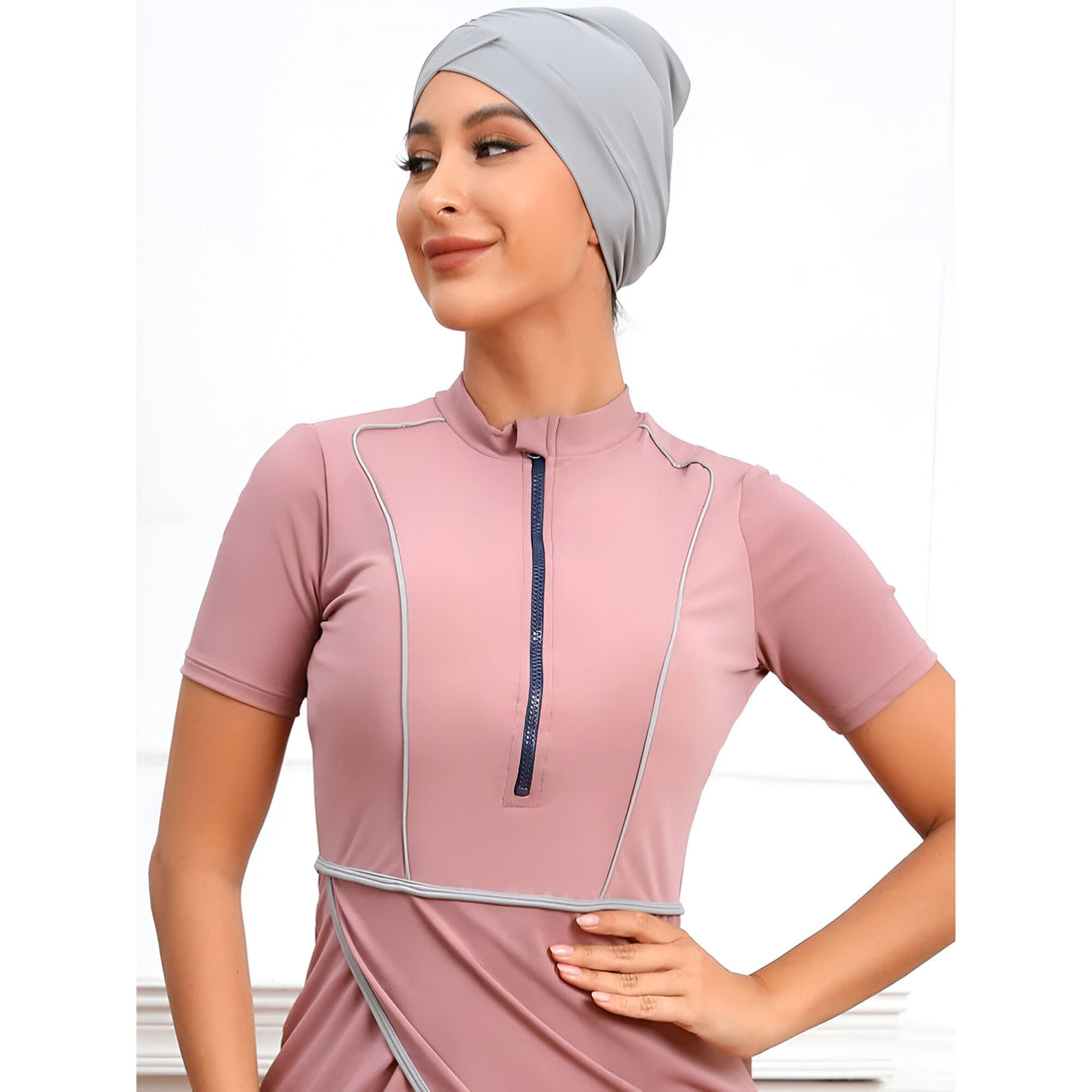 Une femme portant un hijab gris et une robe de bain rose avec une fermeture éclair.  La robe a des détails contrastés en gris et bleu foncé.  Vêtements musulmans pour la plage ou la piscine.