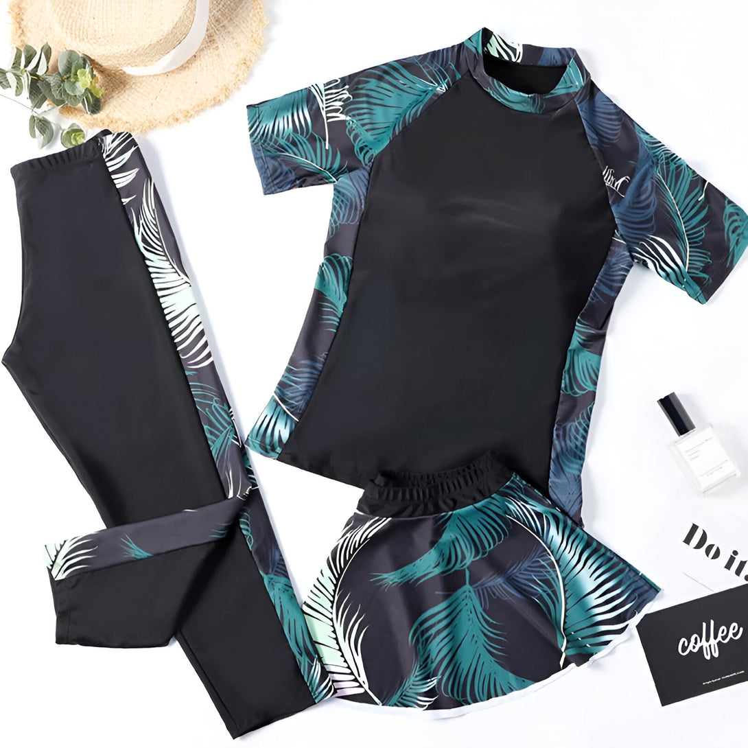 Ensemble de maillot de bain musulman avec un haut à manches courtes, un pantalon long et une jupe courte, tous ornés d'un motif de feuilles tropicales sur fond noir.