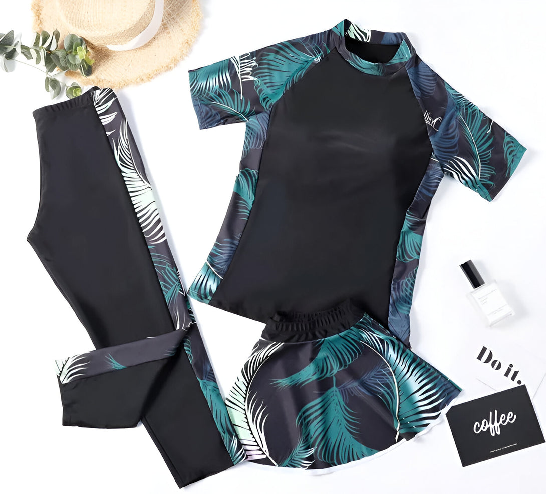 Ensemble de maillots de bain musulmans pour femmes avec un haut à manches courtes, un pantalon long et une jupe, tous imprimés de feuilles tropicales sur fond noir.