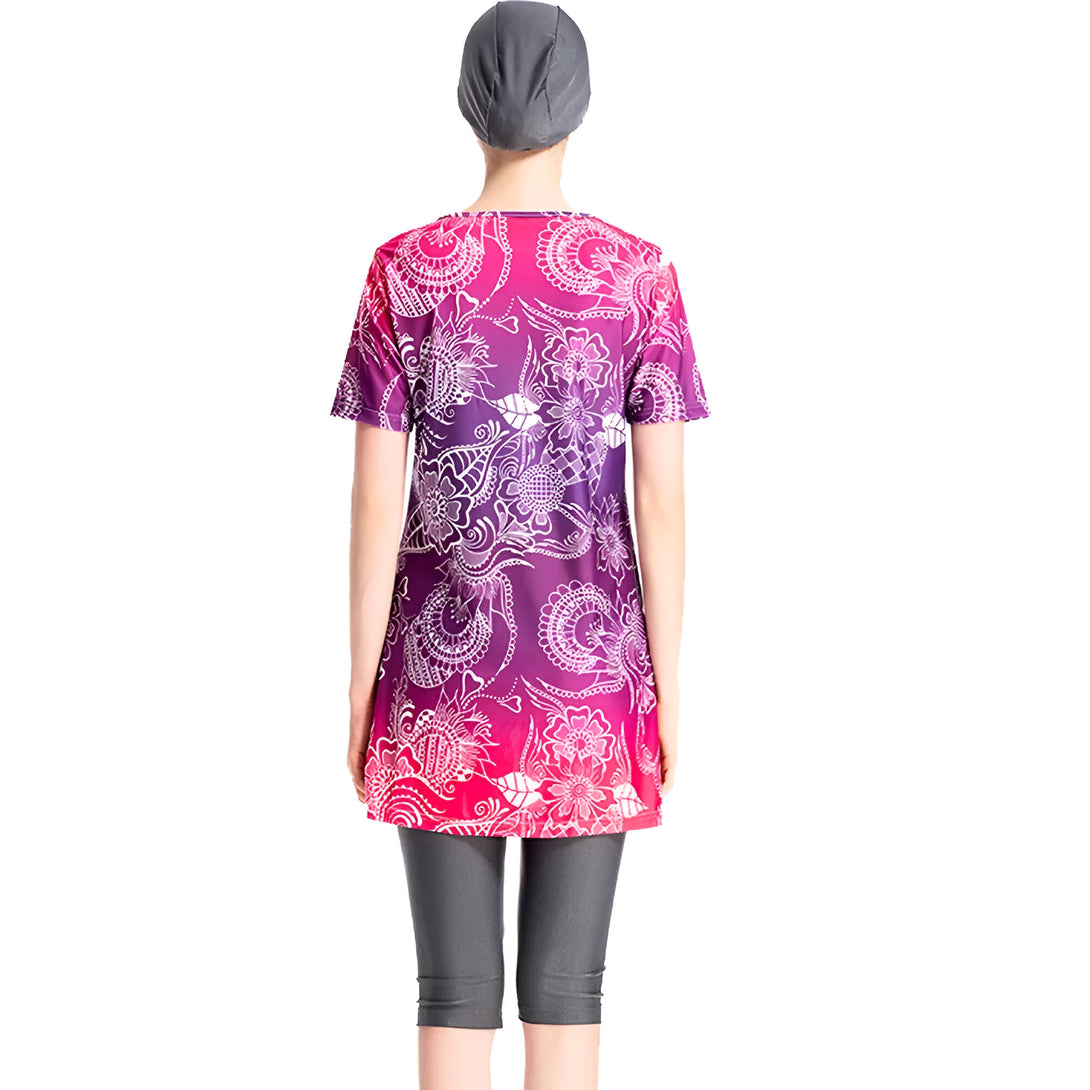 Une femme portant un maillot de bain musulman avec un motif floral en blanc sur un fond violet et rose. Elle porte également un bonnet de bain assorti.