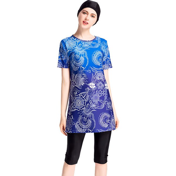 Une femme portant un maillot de bain musulman bleu et blanc avec des motifs floraux. Le maillot de bain est composé d'une tunique à manches courtes et d'un pantalon long.
