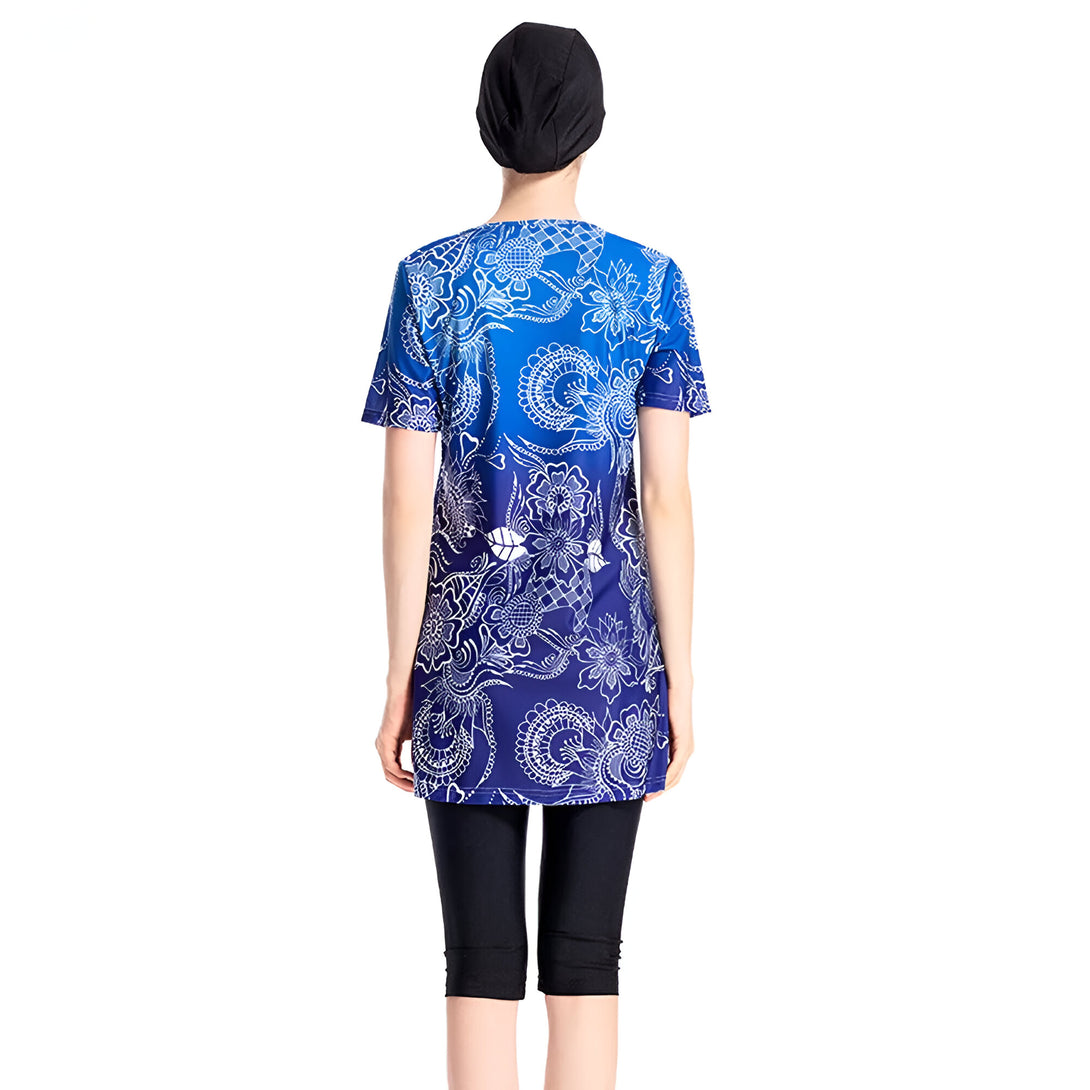 Une femme porte un maillot de bain musulman bleu avec un motif blanc. Le maillot de bain comprend une tunique à manches courtes et un pantalon long. Elle porte également un bonnet noir.