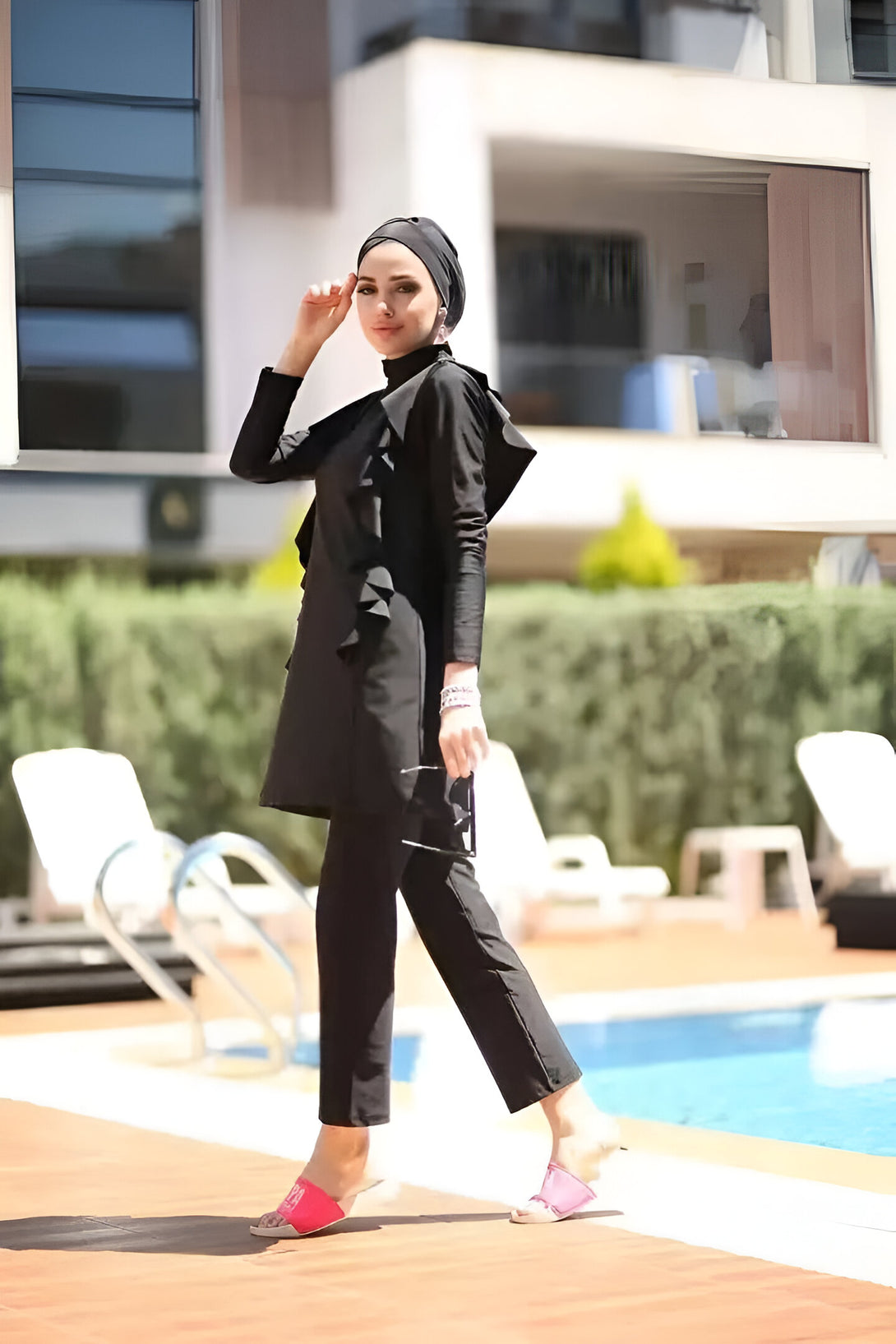 Une femme portant un maillot de bain musulman noir avec un hijab assorti, debout près d'une piscine.  La tenue est élégante et moderne, parfaite pour la plage ou la piscine.