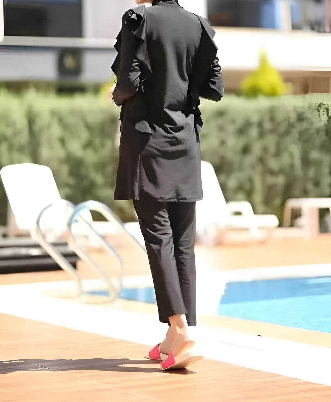 Une femme portant un maillot de bain musulman noir avec des volants au bord de la piscine.