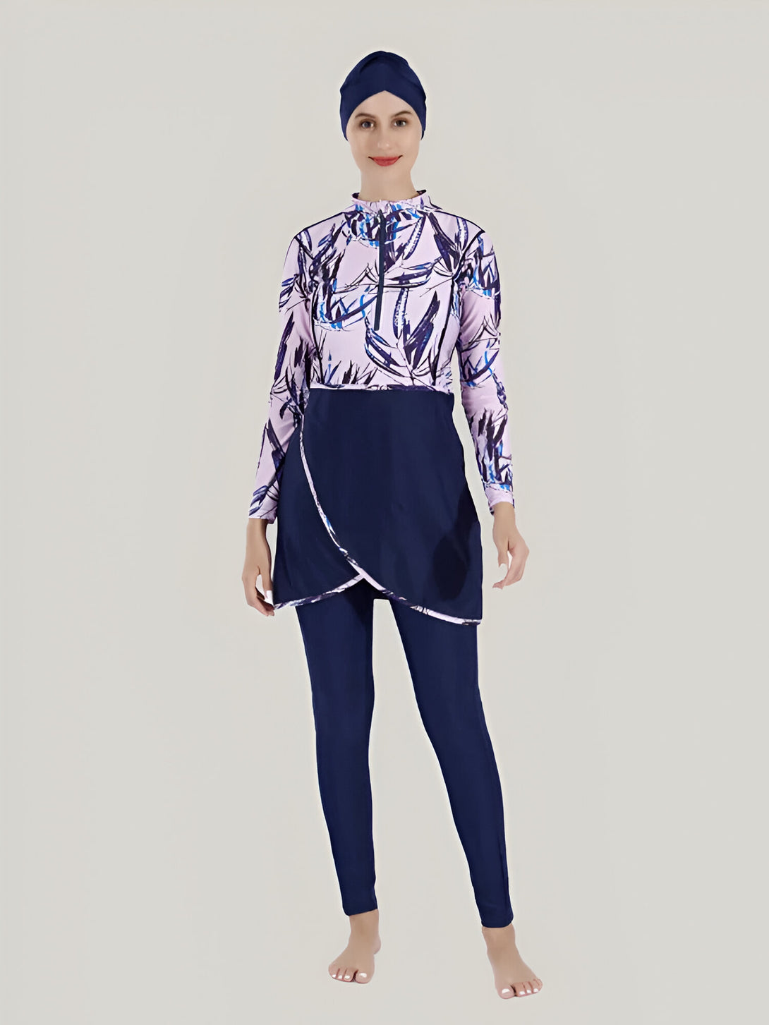 Une femme portant un maillot de bain musulman bleu marine et rose avec un motif floral. Le maillot de bain comprend une tunique à manches longues, un pantalon long et une jupe. La femme porte également un hijab bleu marine.