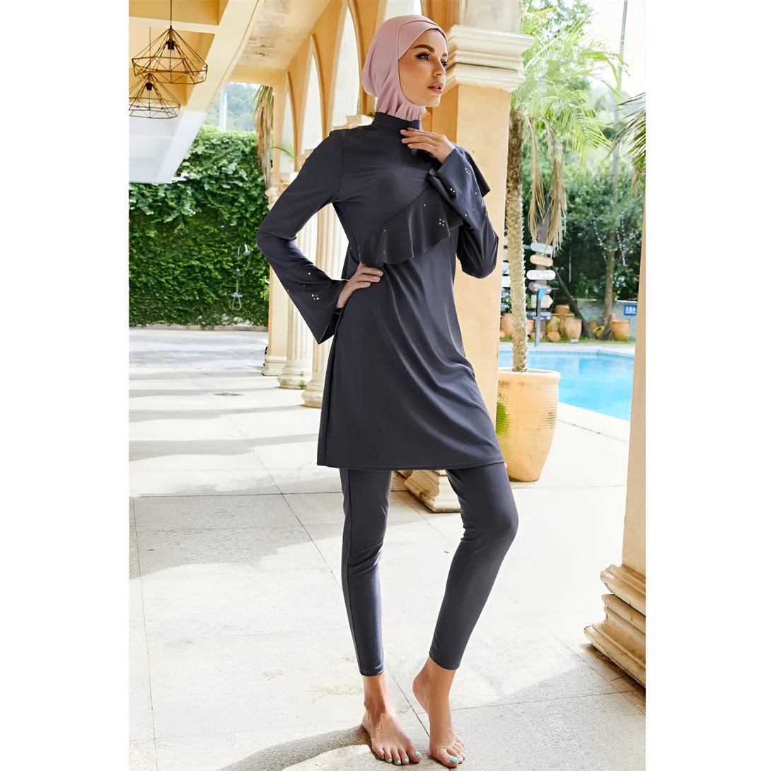 Une femme portant un maillot de bain musulman gris avec un hijab rose. Elle est debout près d'une piscine et porte un hijab rose.
