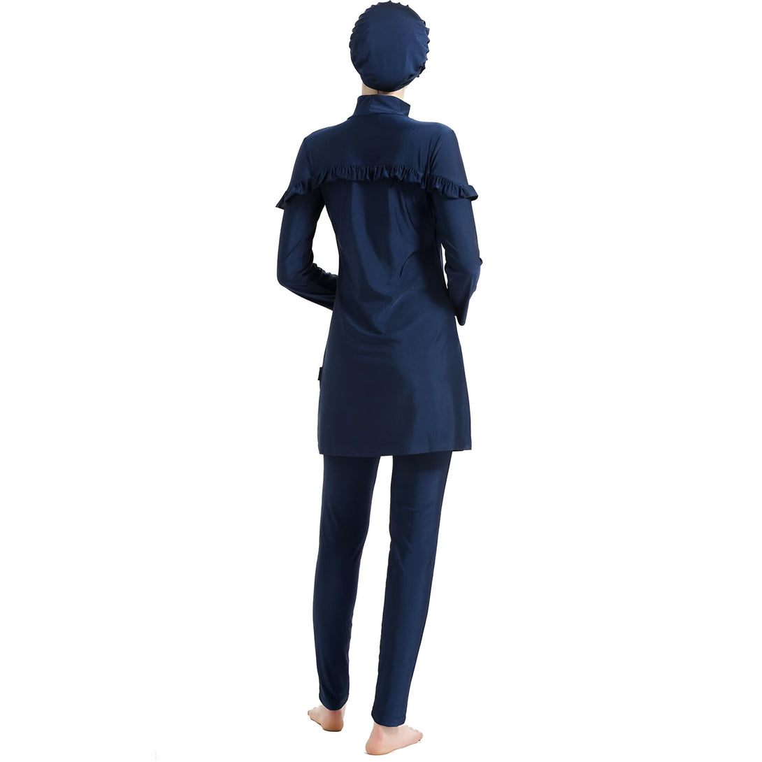 Une femme portant un maillot de bain musulman bleu foncé avec un bonnet assorti. Le maillot de bain comprend une tunique à manches longues avec des volants et un pantalon long.