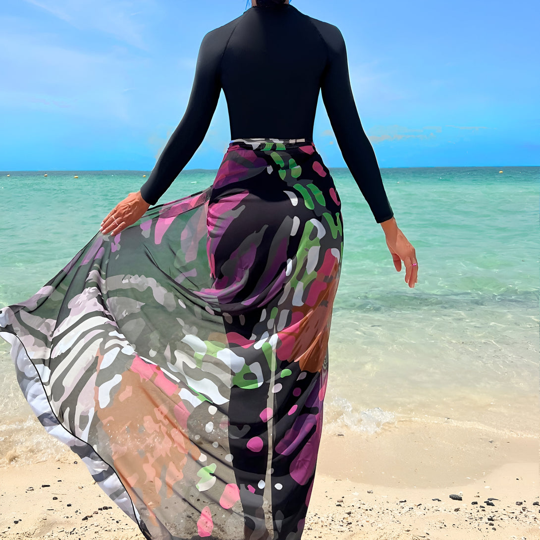 Une femme portant une jupe longue et fluide à motifs colorés sur une plage de sable fin. Le tissu, de couleur noire, beige, rose et vert, offre une touche de style et de modernité à l'ensemble. Cette jupe est idéale pour les femmes musulmanes qui souhaitent se couvrir de manière élégante et tendance.