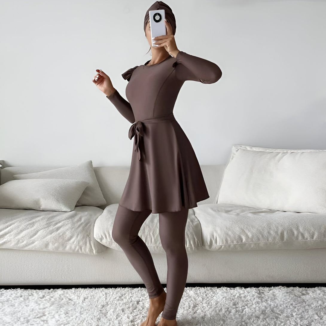 Une femme portant une robe de bain musulmane marron avec une ceinture et un hijab assorti. La robe de bain a des manches longues et une jupe ample.