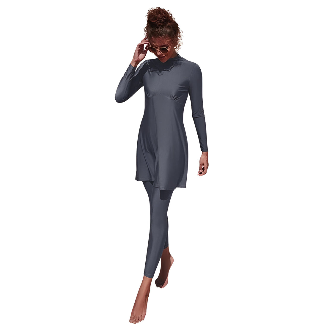 Une femme porte un maillot de bain musulman gris à manches longues et un pantalon long. Elle porte des lunettes de soleil et sourit.  Le maillot de bain est parfait pour la plage ou la piscine.